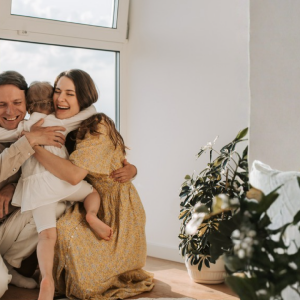 happy mom, dad, and child hugging in their home